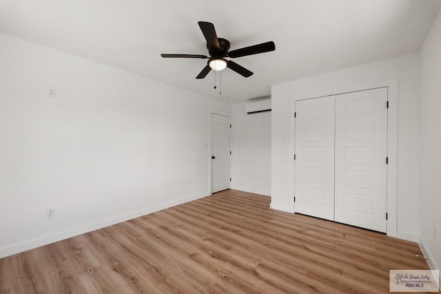 unfurnished bedroom featuring a closet, light hardwood / wood-style floors, a wall unit AC, and ceiling fan