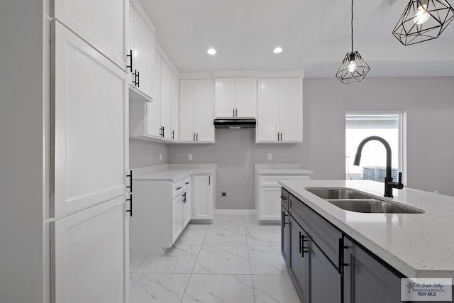 kitchen featuring sink, light stone counters, an island with sink, decorative light fixtures, and white cabinets