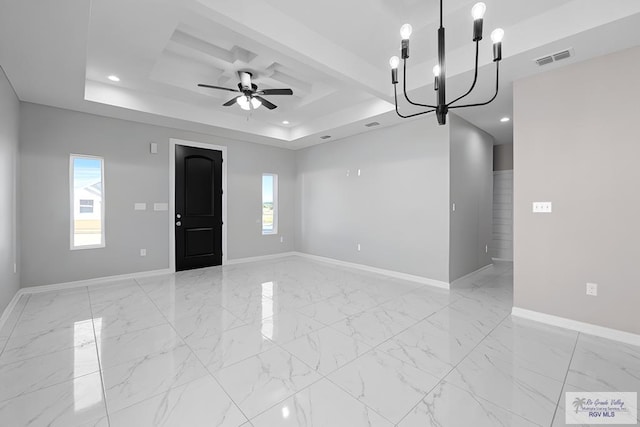 unfurnished room with a raised ceiling, a wealth of natural light, and ceiling fan with notable chandelier