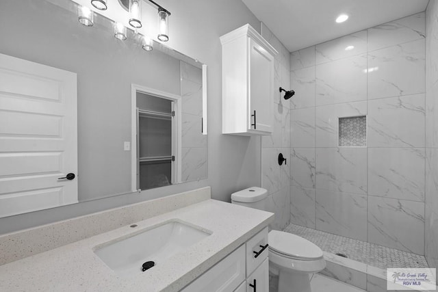 bathroom featuring a tile shower, vanity, and toilet