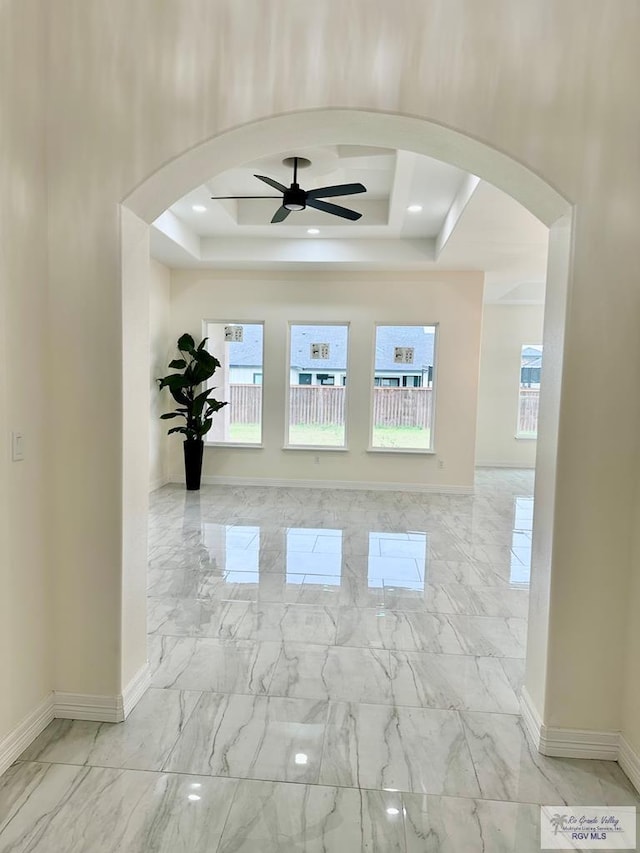 empty room with a raised ceiling, a healthy amount of sunlight, and ceiling fan