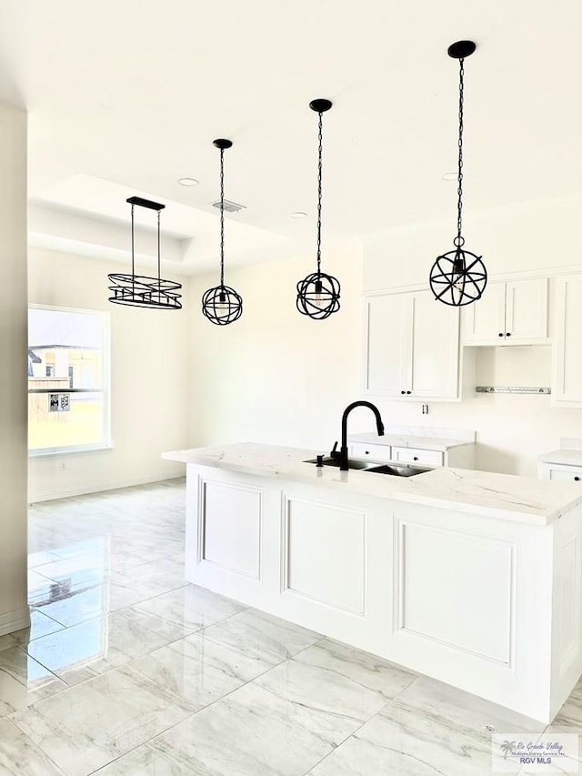 kitchen featuring pendant lighting, white cabinetry, an island with sink, sink, and light stone counters