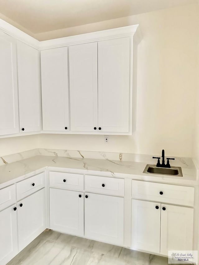 interior space featuring light stone counters, sink, and white cabinets