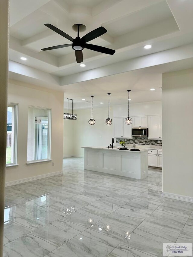 kitchen featuring white cabinetry, decorative light fixtures, a raised ceiling, a kitchen island with sink, and decorative backsplash