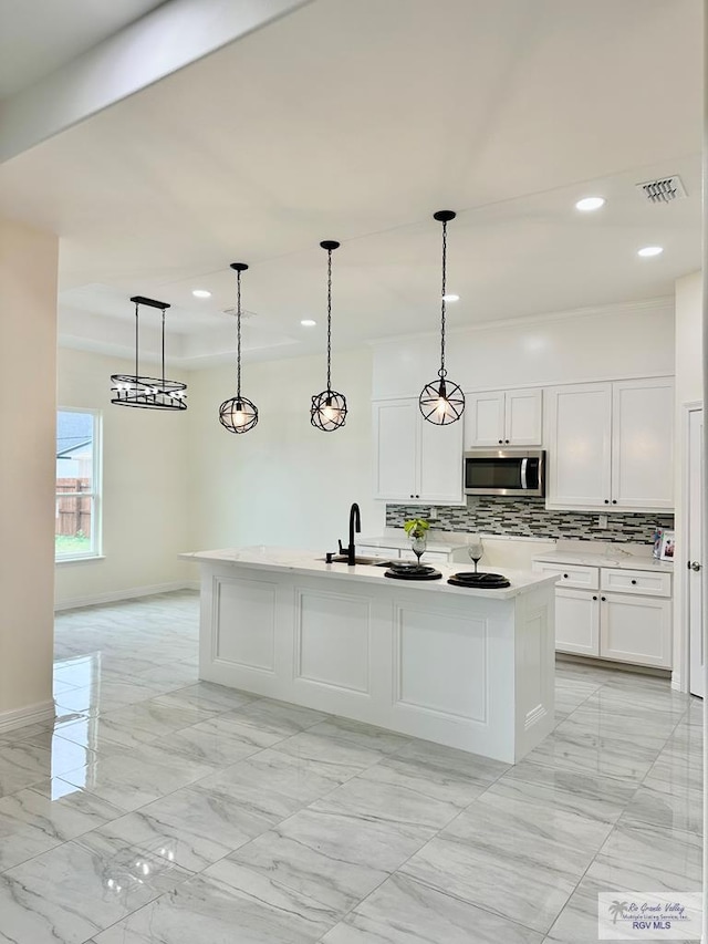 kitchen featuring white cabinetry, decorative light fixtures, an island with sink, and tasteful backsplash