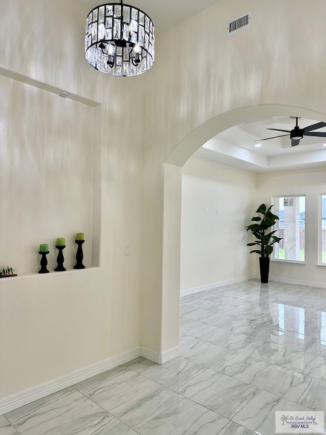 interior space featuring a raised ceiling and ceiling fan with notable chandelier