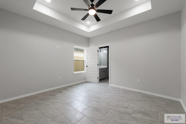 unfurnished bedroom with a raised ceiling, connected bathroom, and ceiling fan