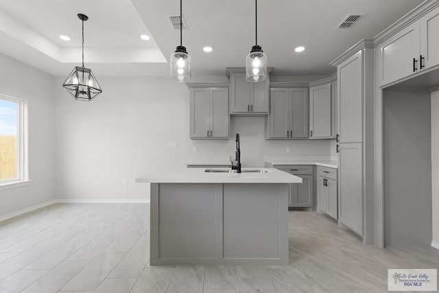 kitchen with pendant lighting, sink, gray cabinetry, an island with sink, and a raised ceiling