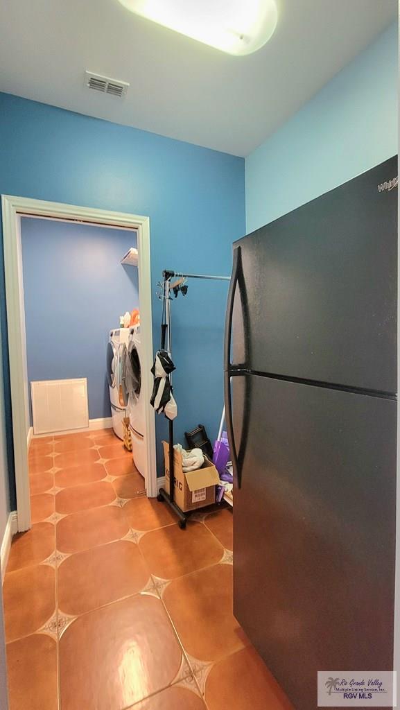 kitchen with tile patterned floors, black refrigerator, and washing machine and clothes dryer