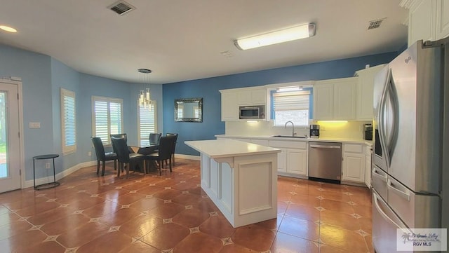 kitchen with sink, decorative light fixtures, a kitchen island, white cabinetry, and stainless steel appliances