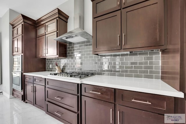 kitchen featuring decorative backsplash, dark brown cabinets, wall chimney exhaust hood, and appliances with stainless steel finishes