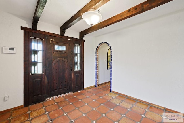 foyer with baseboards, arched walkways, and beam ceiling