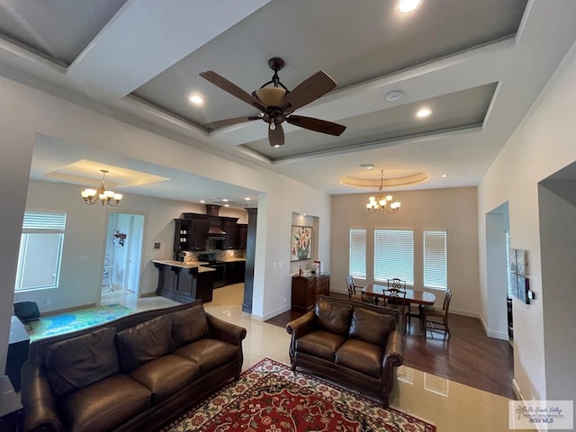 living room with a raised ceiling, light hardwood / wood-style flooring, and ceiling fan with notable chandelier