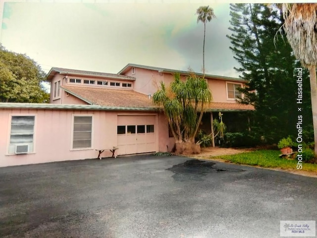 view of front of property with a garage, aphalt driveway, cooling unit, and stucco siding