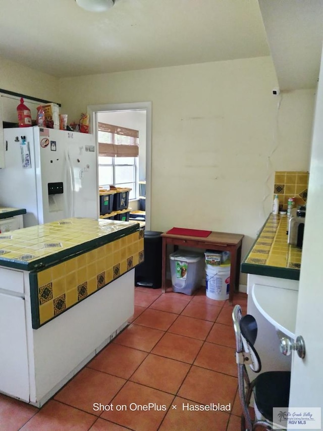 kitchen featuring light tile patterned flooring, white fridge with ice dispenser, light countertops, and white cabinets