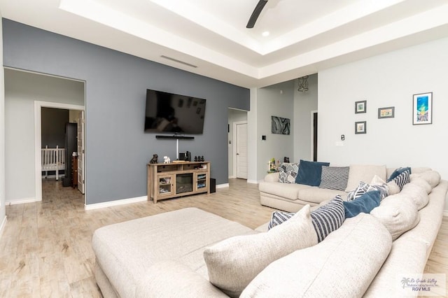 living room with ceiling fan, a raised ceiling, and light hardwood / wood-style flooring