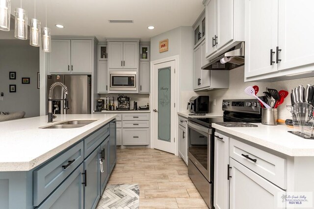 kitchen featuring stainless steel appliances, a kitchen island with sink, sink, decorative light fixtures, and light hardwood / wood-style floors