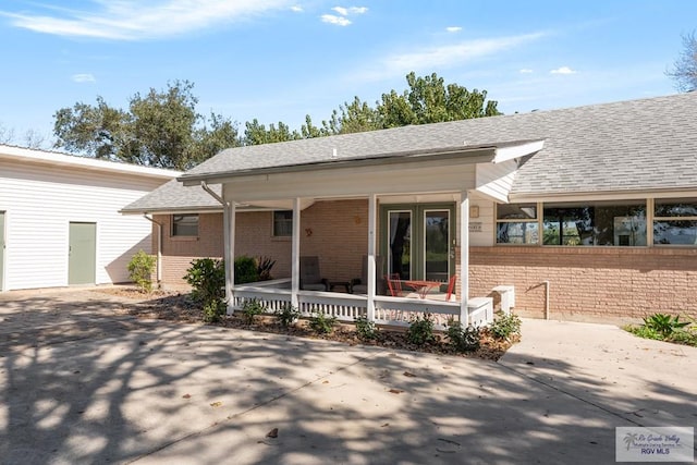 view of front facade featuring covered porch, brick siding, fence, and roof with shingles