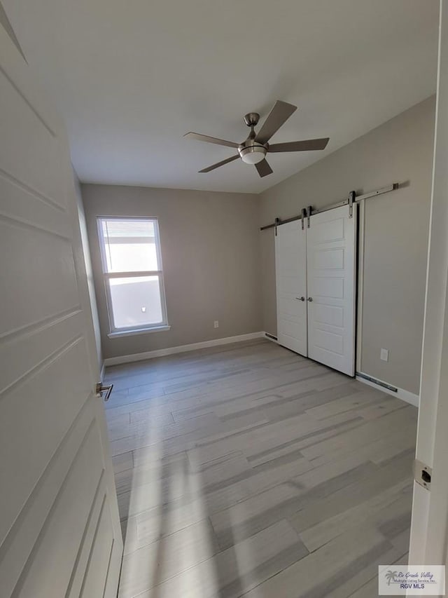 unfurnished bedroom featuring a barn door, ceiling fan, and light wood-type flooring