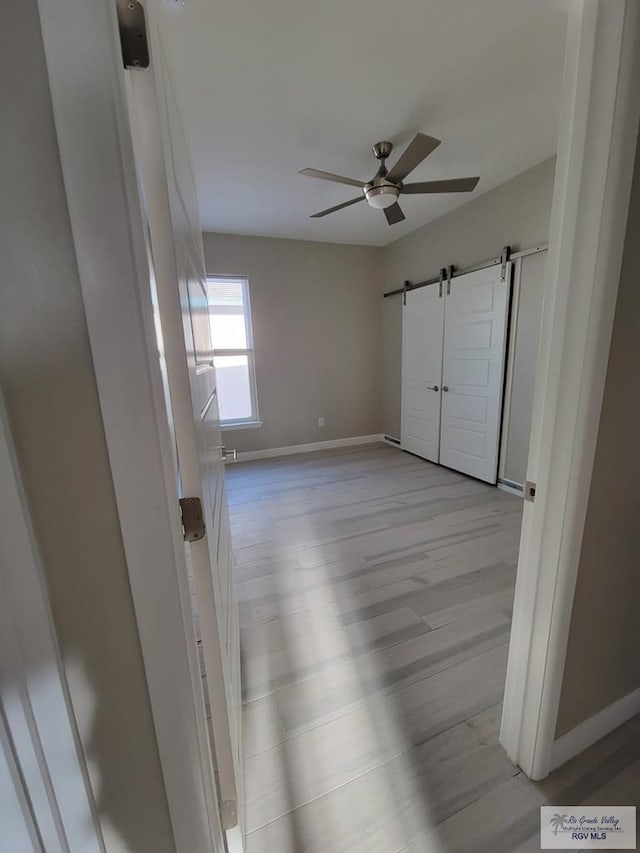 unfurnished bedroom featuring a barn door, light hardwood / wood-style floors, and ceiling fan