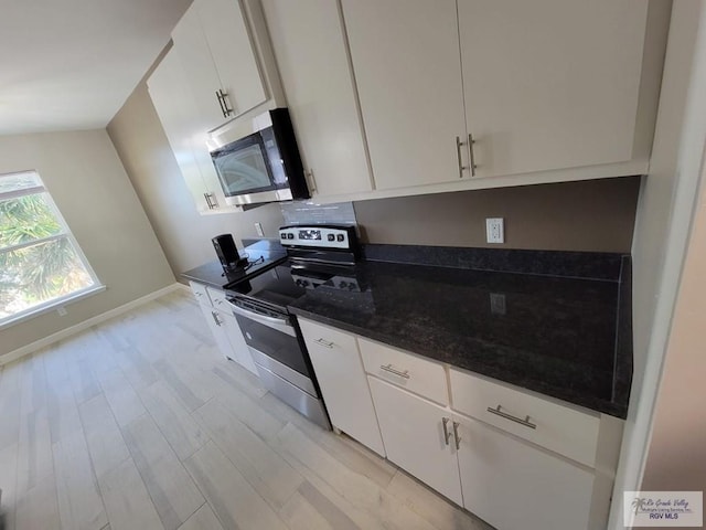 kitchen with dark stone countertops, white cabinetry, appliances with stainless steel finishes, and light hardwood / wood-style flooring