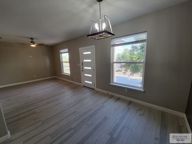 unfurnished dining area featuring wood-type flooring and ceiling fan with notable chandelier