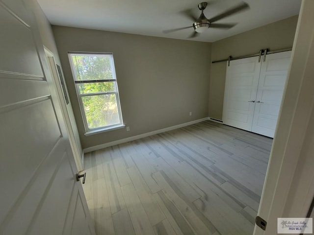 unfurnished bedroom with ceiling fan, a barn door, and light wood-type flooring