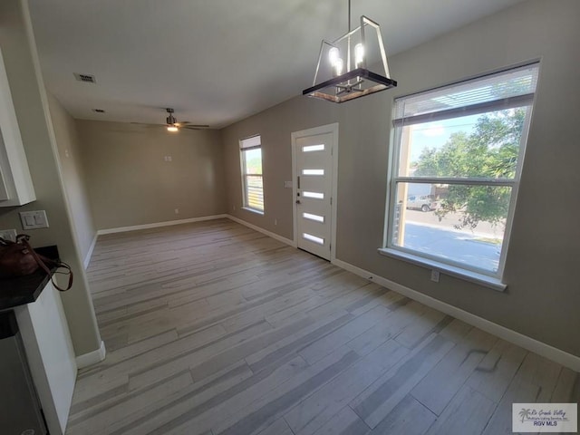 unfurnished dining area featuring plenty of natural light, ceiling fan with notable chandelier, and light wood-type flooring