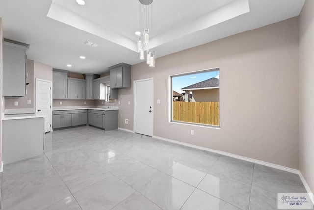 kitchen featuring recessed lighting, baseboards, a raised ceiling, and gray cabinetry