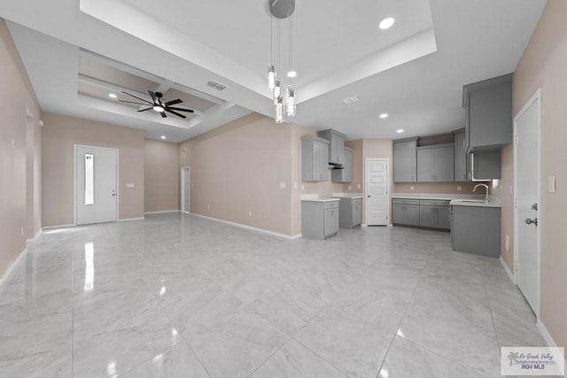 unfurnished living room featuring a tray ceiling, visible vents, baseboards, and a ceiling fan