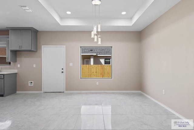 unfurnished dining area featuring a tray ceiling, baseboards, and visible vents