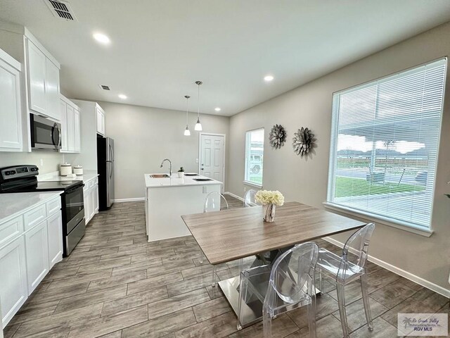 1505 Shavano Dr, Edinburg, TX 78541 - kitchen with stainless steel appliances, a center island with sink, baseboards, wood finished floors, and white cabinetry