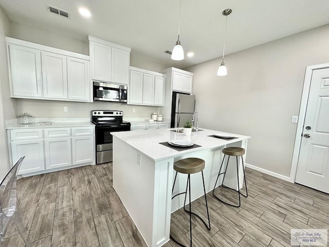 1505 Shavano Dr, Edinburg, TX 78541 - kitchen featuring stainless steel appliances, light wood finished floors, white cabinets, a kitchen island with sink, and recessed lighting