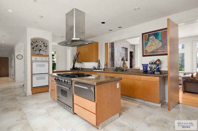 kitchen featuring double oven, a healthy amount of sunlight, high end stove, and range hood