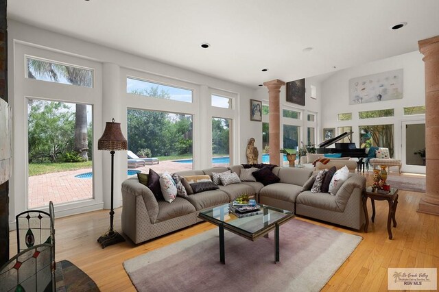 living room featuring a high ceiling, light wood-type flooring, and ornate columns