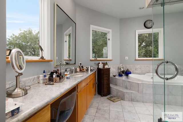 bathroom featuring tile patterned flooring, vanity, a relaxing tiled tub, and a wealth of natural light