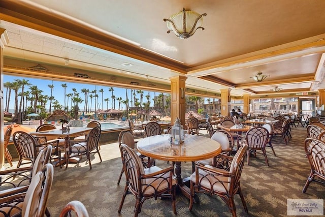 dining area featuring dark colored carpet, a raised ceiling, and decorative columns