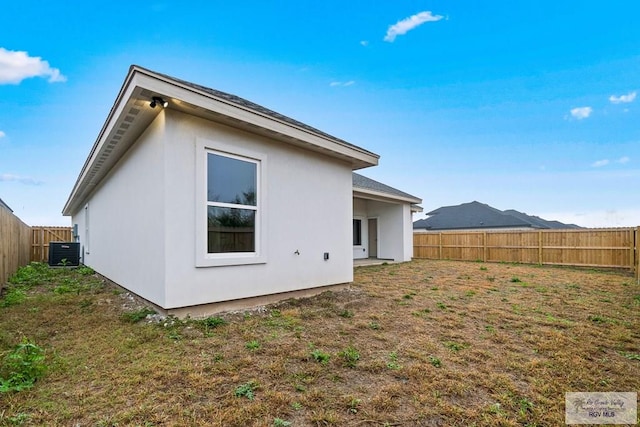 back of house with a lawn, a fenced backyard, central AC unit, and stucco siding