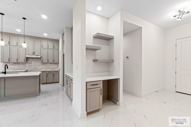 kitchen with tasteful backsplash, baseboards, under cabinet range hood, marble finish floor, and gray cabinets