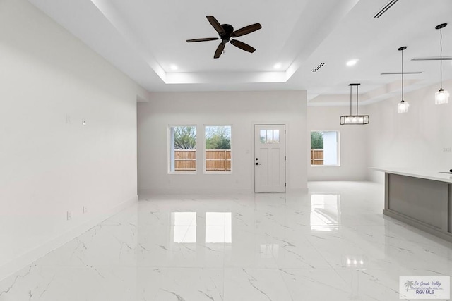 unfurnished living room with visible vents, a ceiling fan, marble finish floor, and a tray ceiling
