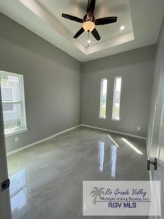 spare room featuring a raised ceiling, a wealth of natural light, and ceiling fan