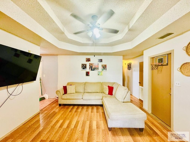 living room featuring a textured ceiling, a tray ceiling, light hardwood / wood-style flooring, and ceiling fan