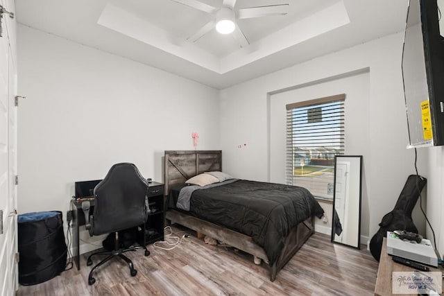 bedroom featuring light wood-type flooring, a raised ceiling, and ceiling fan