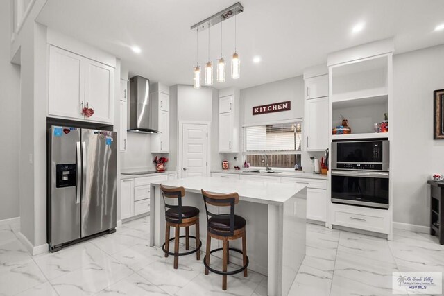 kitchen featuring a center island, white cabinets, wall chimney range hood, hanging light fixtures, and stainless steel appliances