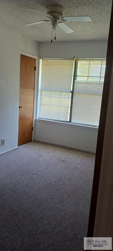 spare room with a textured ceiling, ceiling fan, and carpet