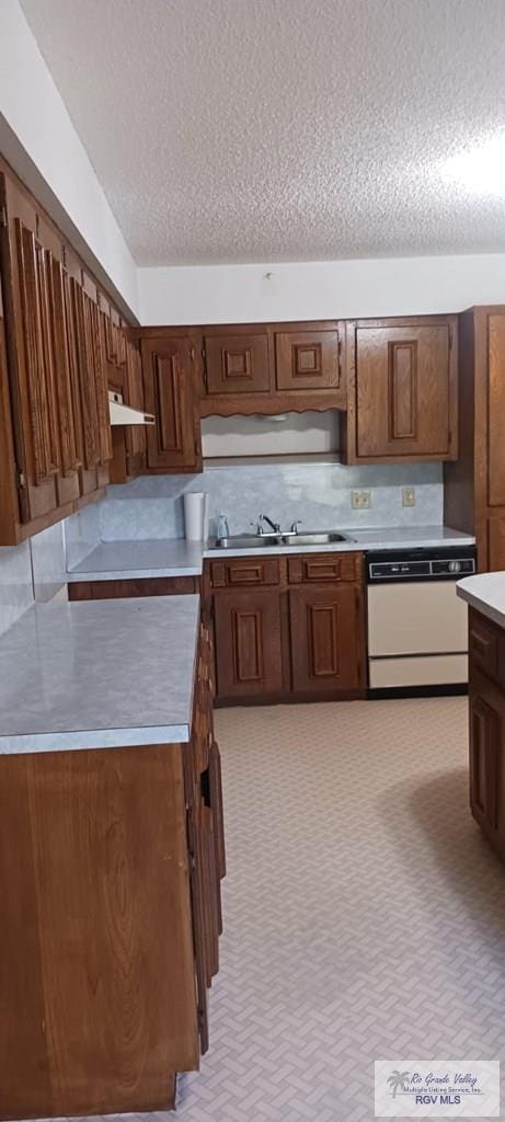 kitchen with a textured ceiling, under cabinet range hood, dishwasher, light countertops, and a sink