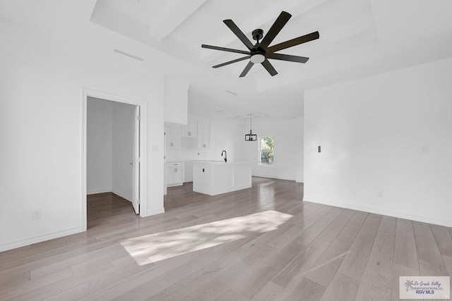 unfurnished living room with ceiling fan, a tray ceiling, sink, and light hardwood / wood-style floors