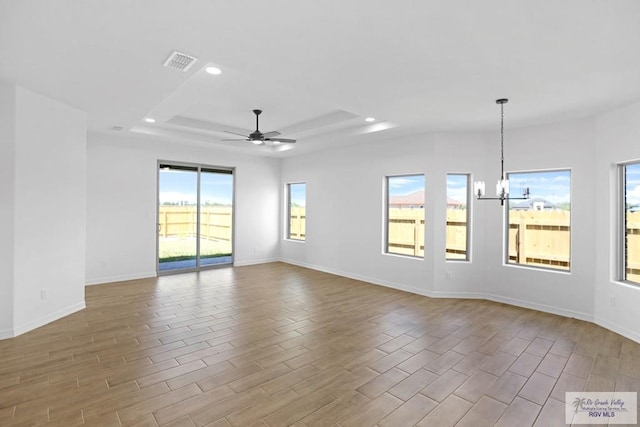 unfurnished room with hardwood / wood-style floors, ceiling fan with notable chandelier, a wealth of natural light, and a tray ceiling