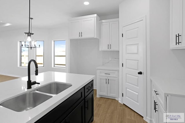 kitchen featuring light wood-type flooring, sink, pendant lighting, an inviting chandelier, and white cabinetry