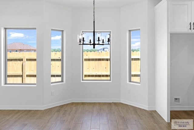 unfurnished dining area featuring an inviting chandelier and light wood-type flooring